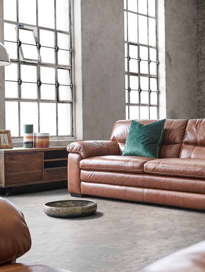Industrial styled brown leather sofa sitting in a loft with grey walls and floor