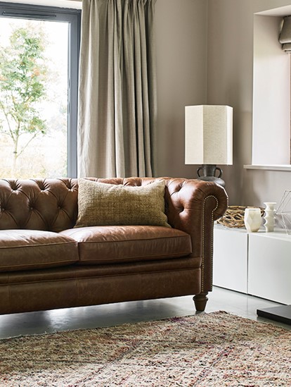 Brown chesterfield sofa in a living room with beige walls and a black fireplace