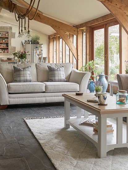 Fabric sofas in light colour with a check patterned armchair next to it sitting in a living room with the kitchen in the back