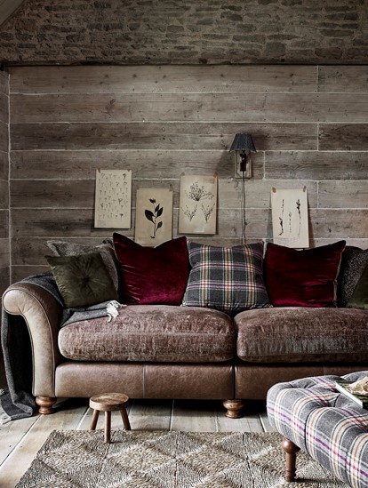 Cosy Alexander & James sofa made of leather and fabric with cushions and throw against a wooden wall